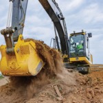 Un operador usa una Excavadora 210P-Tier para recoger tierra de la parte superior de una pila.