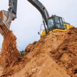 Una Excavadora 250P-Tier descarga tierra en un pozo desde la parte superior de una pila.
